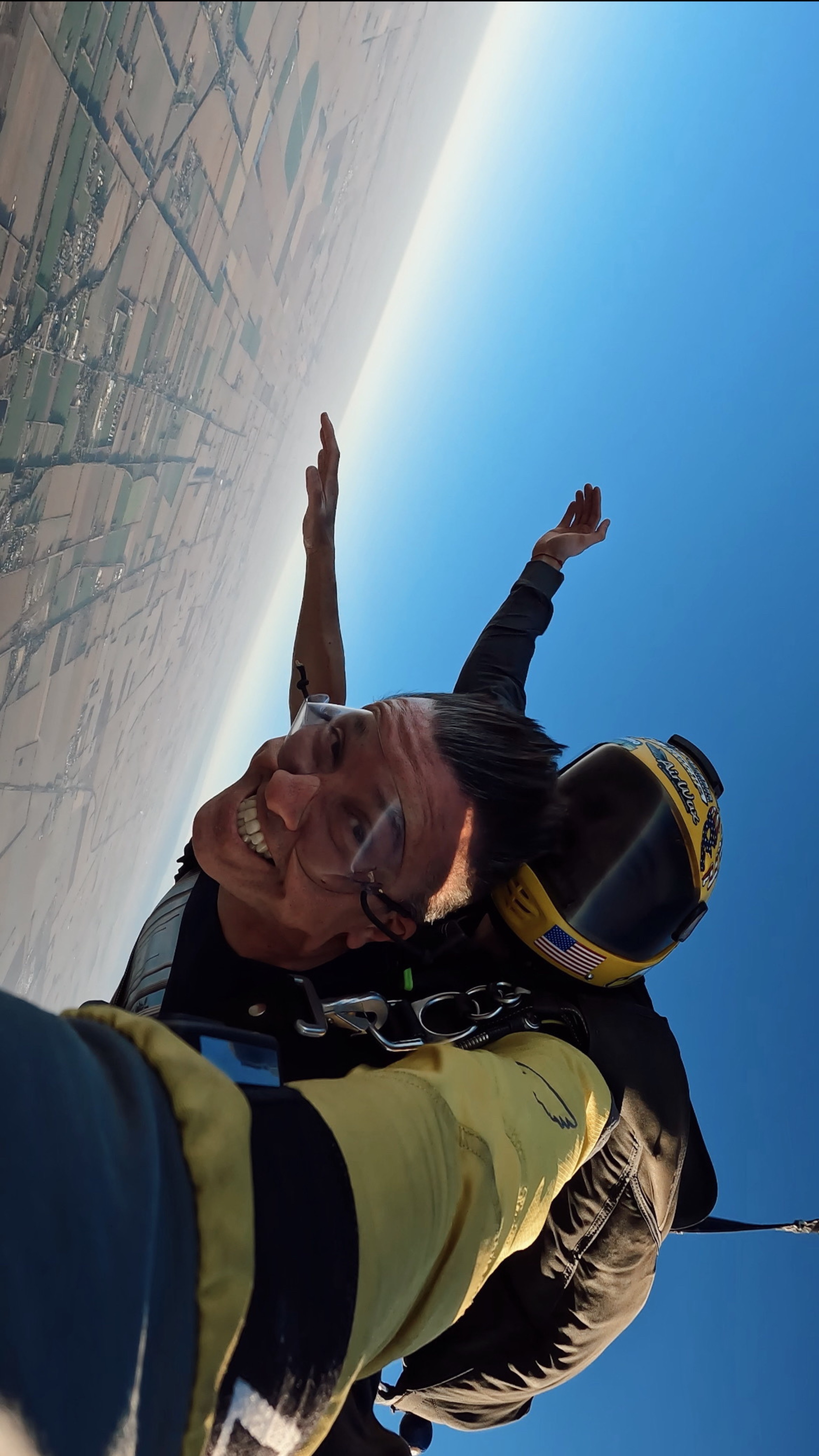 Alumno sonriendo a cámara durante la caída libre, vista de la handycam del instructor